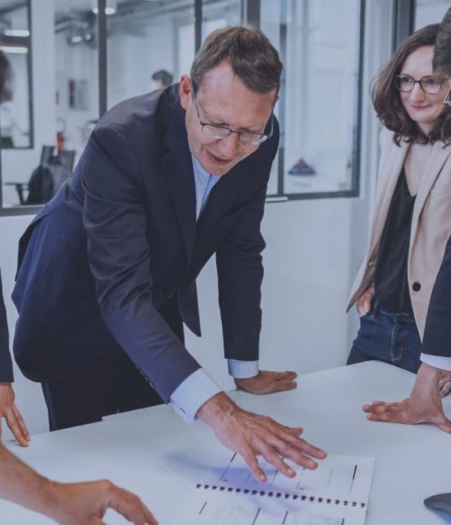 Homme montrant un document à un groupe, illustrant le conseil stratégique Veltys