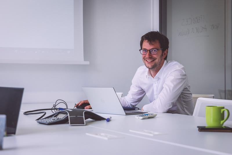 Homme souriant devant son ordinateur portable dans un bureau pour la Stratégie d’offre Veltys